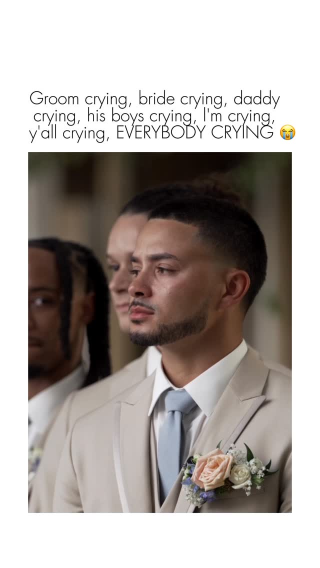 A photo of a wedding featuring three men. The main subject, positioned on the right, is a man in a tan suit with a light blue tie and a rose and floral boutonniere. He is looking to his right with a slightly emotional expression. Beside him are two more men, partially visible, also wearing suits. Text overlayed on top reads "Groom crying, bride crying, daddy crying, his boys crying, I'm crying, y'all crying, EVERYBODY CRYING."