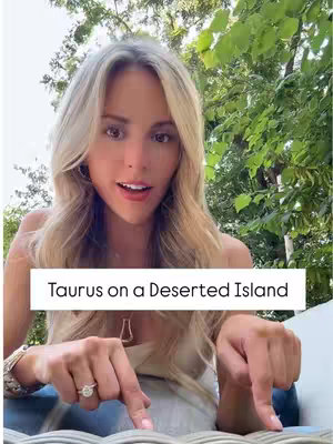 A blonde woman with wavy hair is smiling at the camera, pointing downwards with both index fingers. She is wearing a ring on her left ring finger and has bracelets on her right wrist. The background has green foliage and blurred trees. Over the woman's torso is a white banner with the text 'Taurus on a Deserted Island' in a black sans-serif font.