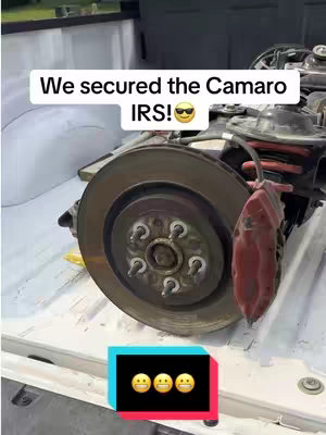 The cover image shows a close-up of a car's rear suspension system, specifically the brake rotor and caliper, likely from a Camaro, placed on a white surface, possibly the bed of a truck. Text overlays indicate the item is being secured as part of a project, and an emoji graphic is added at the bottom.