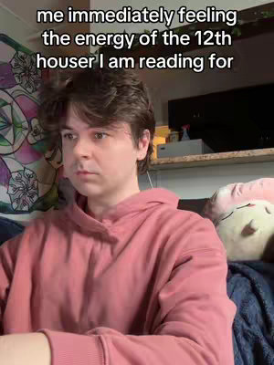 A person with brown hair wearing a pink hoodie is looking towards the left side of the frame. Text is overlaid at the top. The setting includes a colorful tapestry or artwork on the wall, a shelf with various items, and items placed on the bed like pillows and stuffed animals.