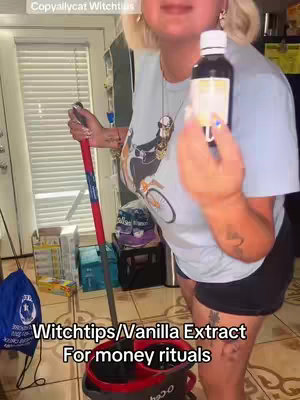 A woman in a t-shirt and black shorts stands in a home setting, holding up a bottle with a white label and a mop. The background includes a window with blinds and various household items.