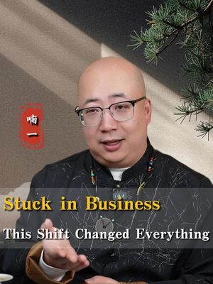 A man with glasses is the central focus, positioned in the center of the frame, and is bald on top with a friendly expression. Overlaid are texts in yellow, while other visual elements of Chinese symbols are present in the upper left corner of the image. The background is a mix of neutral and wood tones, with some green foliage visible on the upper right.