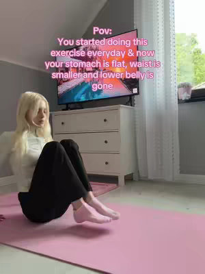 A woman is sitting on a pink yoga mat in a room, with a TV in front of her. The woman has long blonde hair and is wearing a white top and black pants. Text is overlaid on the image in pink.