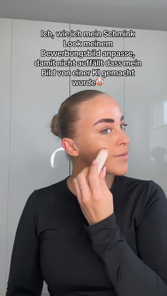The cover image is a close-up selfie of a woman applying makeup. She is holding a makeup stick to her cheek, and her skin has a highlighted, contoured appearance. The top of her head and hair, styled in a bun, are included in the frame. Overlayed text is at the top of the image.