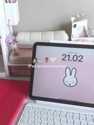 An iPad with a white Magic Keyboard is open on a desk. The iPad displays the time, a Miffy bunny image, and the text: 'iPad accessories haul'. Various accessories and stationery items sit in the surrounding area.