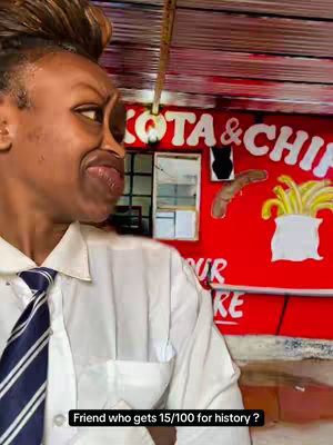 A woman with dark skin, her hair styled up, is looking sideways with a playful expression, her mouth slightly open as if surprised. She is wearing a white collared shirt and a striped tie. Behind her is a red wall with a sign advertising food, including the words "KOTA & CHIP", along with illustrations of a sausage and fries. The woman's expression indicates she is looking at or interacting with something off-camera.