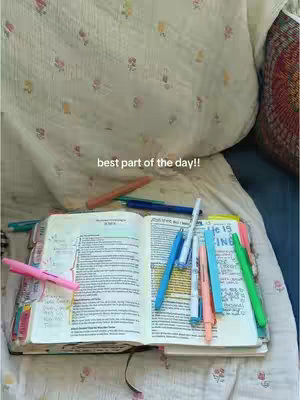 A view of an open Bible with various colorful pens and markers laid across the pages, resting on a patterned surface, possibly a blanket or bedspread. The words 'best part of the day!!' are written at the top