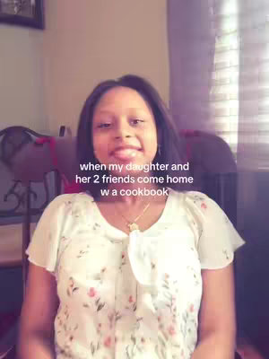 A woman with long dark hair is smiling and looking at the camera. Text overlay on image says 'when my daughter and her 2 friends come home w a cookbook'. The woman is wearing a white blouse with small pink floral patterns.