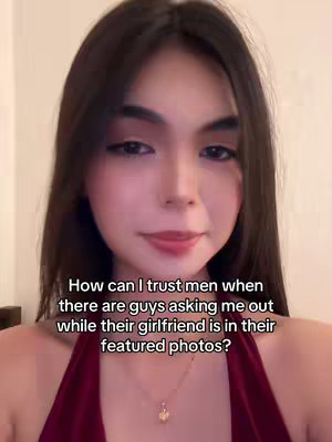 A young woman with long dark hair is centered in the frame, looking directly at the viewer. She wears a deep red halter top and a gold necklace. Text is overlaid on the image, in white font. The background is a soft, neutral color, suggesting an indoor setting.