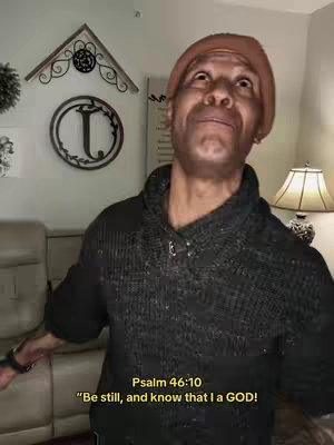 A man wearing a beanie and a sweater is looking upwards, with a quote overlaid at the bottom of the image. The background shows a living room setting with wall decor and a lamp.
