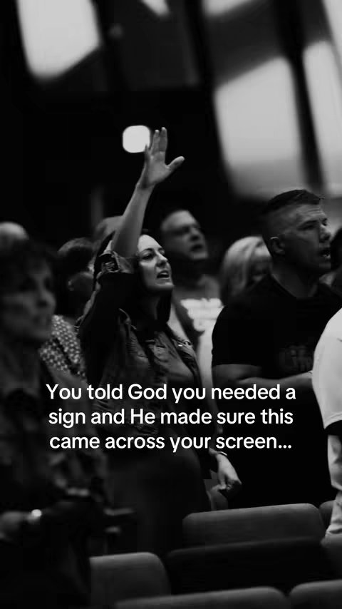 A black and white image capturing a worship service. A woman with her arm raised is the focal point, set against a blurry background of more people in the congregation.