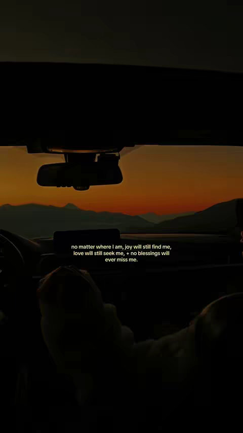 Interior shot of a car at sunset, viewed from the driver's perspective. The foreground shows the steering wheel and dashboard in shadow. The background features a vibrant sunset with shades of orange and red behind silhouetted mountains. Text overlayed at the bottom provides a motivational quote.