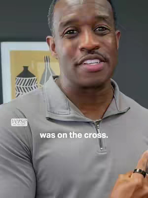 A medium shot shows a black man with short, neatly styled black hair and a mustache, looking directly at the camera and speaking. He's wearing a gray zip-up jacket. The background is out of focus, with hints of artwork or wall decor. Text overlay on the lower third completes the video's hook.