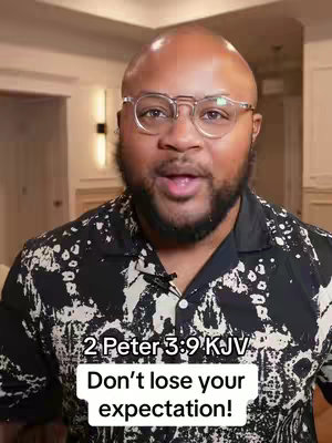 A medium shot features a bald Black man with a neatly trimmed beard and glasses, speaking directly to the camera. He is wearing a black and white patterned shirt, and the background includes a glimpse of a room with neutral-colored walls and simple interior elements. Text overlays at the bottom provide a Bible verse reference and a motivational message.