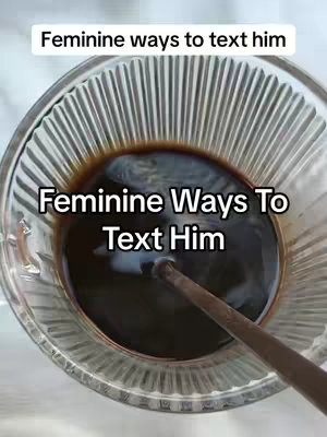 The image shows a close-up view of a clear glass bowl filled with a dark brown liquid, in which a dark colored stirrer is placed. The bowl has a ridged design around its rim. Above the bowl is text overlay that reads: 'Feminine ways to text him'. The background is blurred, and the overall composition is simple with a focus on the liquid.