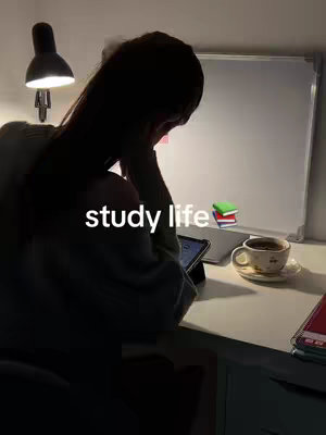 A dimly lit image showing a person, seen from the back, studying at a desk. The person is partially obscured by shadows with their head resting on their hand. On the desk are a tablet, a cup of coffee, some books, and a study lamp. The words 'study life' are overlaid on the image.