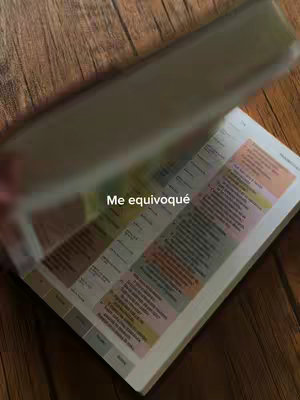 The image shows a book with pages being turned.  In the foreground, a hand appears to be flipping through the pages of a book with text. The background shows the image of a wooden table