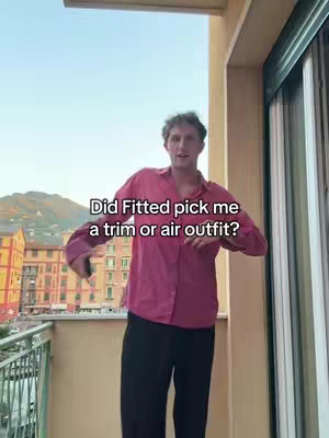 A man stands on a balcony, with a cityscape and mountain visible in the background. He wears a pink shirt and black pants. Text overlay asks if the app 'Fitted' picked his outfit.