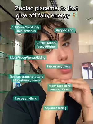 A selfie-style image with a fair-skinned person, with dark hair, and multiple face piercings. The individual is positioned slightly off-center, resting their chin gently on their hand which is supporting their face. The background appears to be an interior space. The image is overlayed with various text elements in green boxes, pointing towards different facial regions. The text labels are related to zodiac signs and placements.