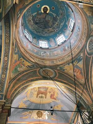 The cover image presents a detailed view from inside a church. The primary focus is on the domed ceiling, which is adorned with intricate frescoes and paintings. The ceiling is a vibrant blue, with religious figures depicted in the central portion. The walls of the church are decorated with more religious art, featuring various figures and scenes, all composed with detailed brushstrokes and a muted color palette. The composition is symmetrical, drawing the viewer's eye upwards to the central dome.