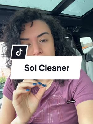 The video's cover image features a woman in a car, appearing to film herself. Above her is the car’s sunroof. A white rectangle saying 'Sol Cleaner' sits centrally, a TikTok logo in the upper left corner. She wears a purple shirt and has dark curly hair. Her nails are painted blue, and the bottom right of the image shows the word 'علي'.