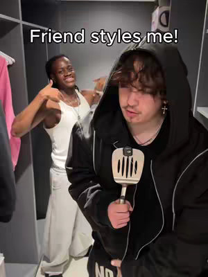 The cover image shows two young men in a closet. The man in the foreground, wearing a hooded jacket, is holding a spatula up. His friend, in the background, gives a thumbs up. The text overlay reads 'Friend styles me!'