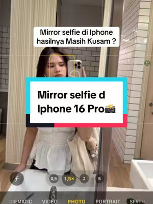 The cover image shows a mirror selfie taken in a bathroom. A young woman, visible from the chest up, is holding a phone in front of her face. She is wearing a white top with a tiered design. The background includes the bathroom mirror, a sink, and a tiled wall. Text overlays, in a mix of English and Indonesian, are placed over the image, indicating the video's theme is related to taking clear mirror selfies on iPhones.