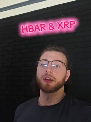 A man with glasses is centered in front of a black brick wall looking at the camera. Above his head is a pink neon sign that reads 'HBAR & XRP'.
