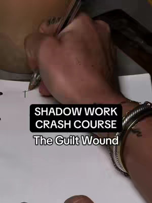 The image shows a close-up of a person's hand writing on a piece of paper.  A text overlay at the bottom shows the title : "Shadow Work Crash Course". A bracelet is also visible. The overall composition is focused on the hand and the text, with a dark background and minimalist color scheme.