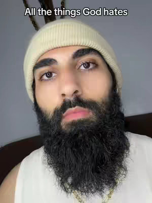 A close-up shot of a man with a thick, dark beard and a cream-colored beanie. The text overlay reads, 'All the things God hates,' set against a plain background.
