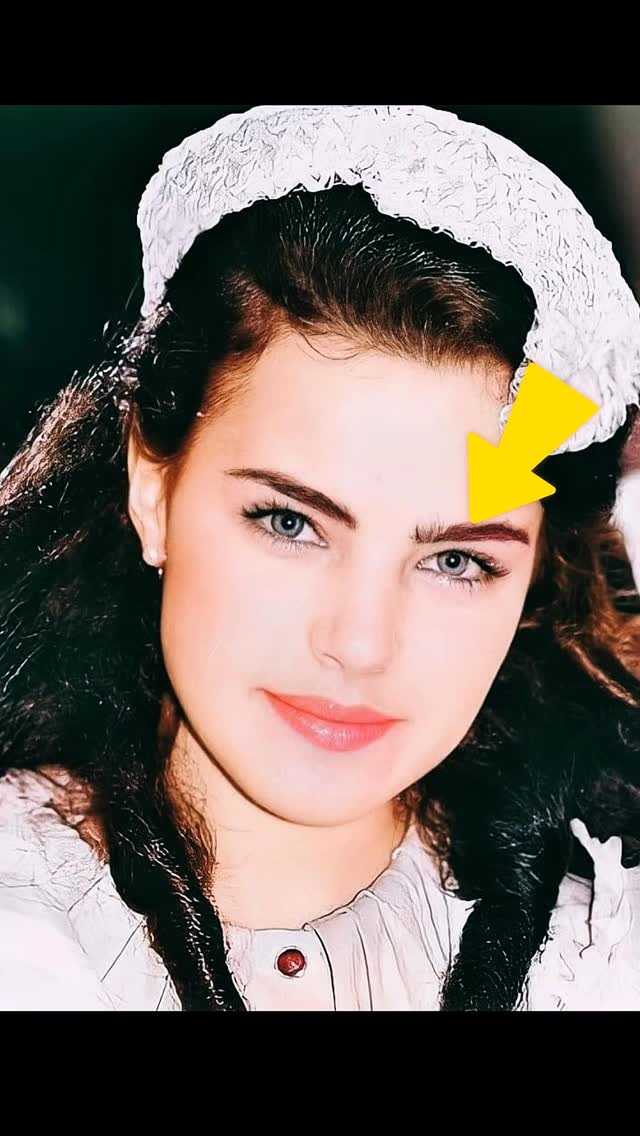 A close-up image of the face of a woman with dark hair and blue eyes. She wears a white lace head covering and a white top with a red button detail. A yellow arrow points to her eyebrow. The image has a vintage style with a softly blurred background.