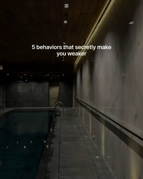 The image captures a wide, dimly lit interior space, possibly a luxurious indoor pool area. The main focus is a rectangular pool filled with dark, reflective water. Next to the pool there's a walkway with a low, metallic railing. The walls are a combination of dark, textured panels and lighter, marble-like surfaces, creating a contrast. Overhead, a series of recessed lights provide a subtle glow, and the overall atmosphere is subdued and sophisticated. Text overlayed suggests content related to personal growth or self-improvement.