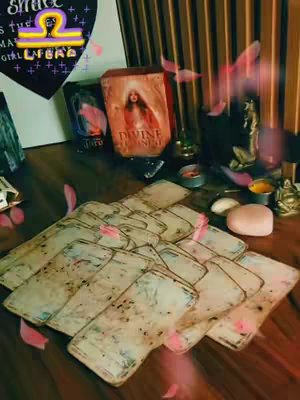 The cover image presents a mystical scene with a collection of tarot cards fanned out on a wooden surface. Surrounding the cards are several decks, candles, and decorative items. Delicate pink elements appear to float around, suggesting an ethereal, almost magical context. The image has a warm, inviting color palette dominated by soft lighting.