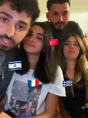 The cover image is a selfie-style shot of four people, composed of two men and two women, seemingly indoors under warm lighting. The composition has the people close together, and four national flags stickers are overlaid on the image. The flags are of Israel, France, Turkey, and Greece. The people face the camera, with varying facial expressions.