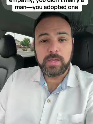 A man with a beard and a white shirt is seated inside a car, looking directly at the camera. The background includes a blurred view of an outdoor setting and dark car seats. The image is well-lit with a focus on the man's face.