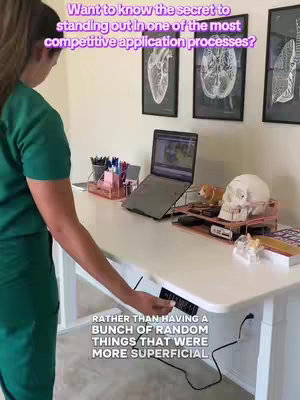 A woman in green scrubs stands at a white adjustable desk in a room with anatomical art on the wall. Overlay text in the image asks how to stand out in a competitive college application process. The desk has a laptop, a skull, and supplies.