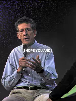 A man wearing a light blue button-up shirt is holding a microphone and speaking, his hand gestures and facial expressions indicating he is in the middle of a presentation or discussion. The background is a dark, possibly indoor setting with some abstract light effects, and the text overlay 'I HOPE YOU AND I' floats above the man's head. The composition is a medium shot from the chest up.