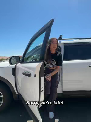 A woman stands outside a white SUV with the door open, the blue sky is above her