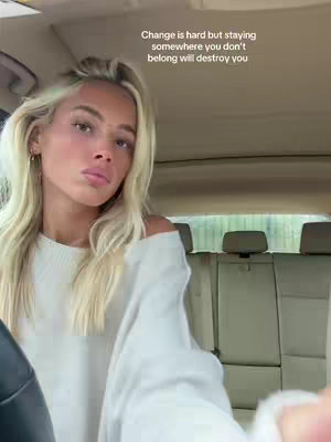 A woman with blonde hair sits inside a car, looking toward the camera. Text overlayed at the top reads, "Change is hard but staying somewhere you don't belong will destroy you."