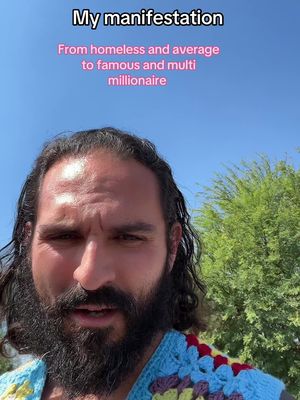 A selfie-style shot featuring a man with a long black beard and long dark hair, standing outside with a bright blue sky in the background. He is wearing a colorful knitted top and looking directly at the camera. Text overlays are present.