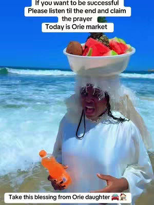 A woman wearing a white outfit with a head covering and a bowl of fruit balanced on her head stands on a beach with waves and blue sky in the background, holding an orange bottle and gesturing towards the viewer. Text overlays are added to the image.