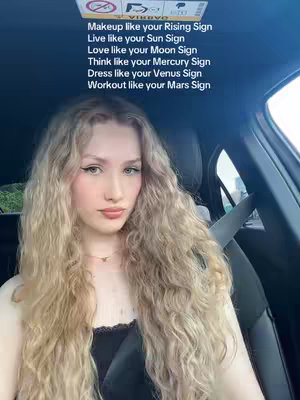A selfie-style shot taken from inside a car, featuring a young woman with long, wavy blonde hair. She's looking directly at the camera with a slight smile and wearing a delicate necklace. Text overlays are positioned above her head, listing various astrological-themed rules.
