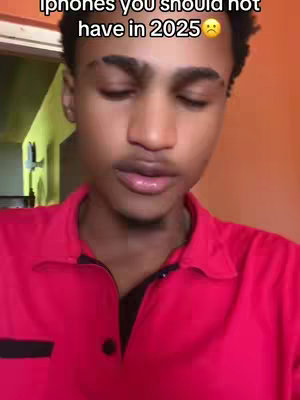 A young man with short, dark hair is centered in a video frame with an orange-colored wall in the background. He is wearing a vibrant red polo shirt. The video appears to be taken from a medium close-up angle.