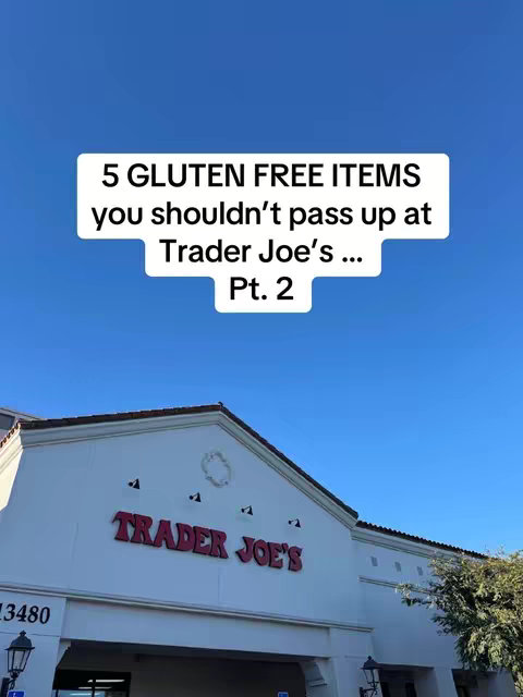 A daytime shot of a Trader Joe's store entrance. The building is white with a red Trader Joe's logo in bold letters above the entrance, under a bright blue sky. A text overlay in a white box states "5 Gluten Free Items you shouldn't pass up at Trader Joe's... Pt. 2". The image suggests a video about gluten-free product recommendations.