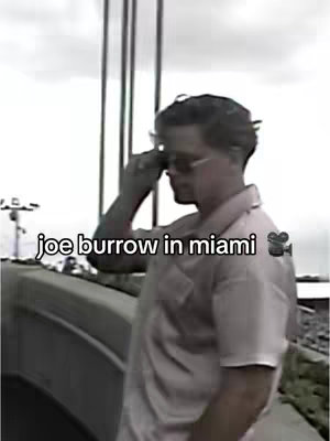 The image shows a man, Joe Burrow, wearing sunglasses and looking away from the camera. He's standing on a bridge or elevated walkway, with a blurry background suggesting an outdoor setting.