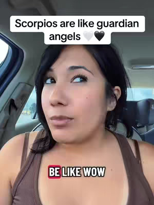 A woman in a brown tank top sits inside of a car and looks up. Above her head, text reads "Scorpios are like guardian angels" with a white and black heart icon. Overlay text at the bottom says "BE LIKE WOW".