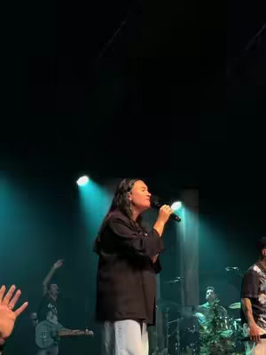 The cover image shows a woman singing into a microphone on a stage with a band in the background. The lighting is primarily green and blue, highlighting the performer and the band. Some people's hands are also visible in the front.