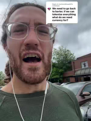 A man with glasses and a beard is looking directly at the camera with his mouth open. He's wearing a green long-sleeve shirt and white wired earbuds. Behind him are parked cars and a building.