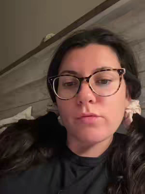 The cover image features a woman in front of what seems to be a wooden wall, possibly a headboard. She is wearing glasses and a black shirt, and has her dark hair pulled back into pigtails. She has a neutral expression, looking towards the camera.