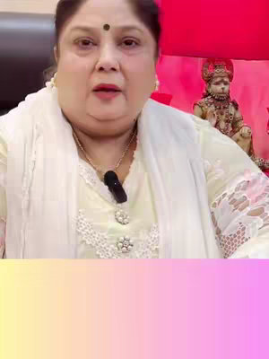 The cover image shows a middle-aged woman with fair skin and a dark bindi between her eyebrows. She wears a light yellow outfit with a white scarf around her shoulders and has a gold necklace with a pendant. Behind her is a statue of a deity.